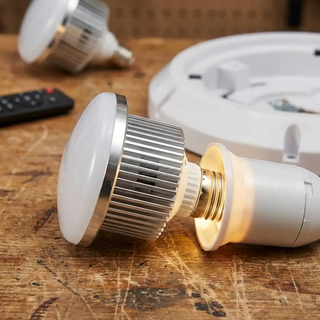 Close-up of a light bulb being screwed into a socket on a wooden workbench with plastic housing in the background.